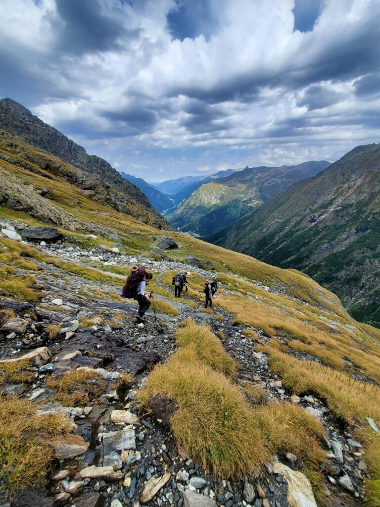 Hikers on a scenic mountain trail with dramatic skies above.
