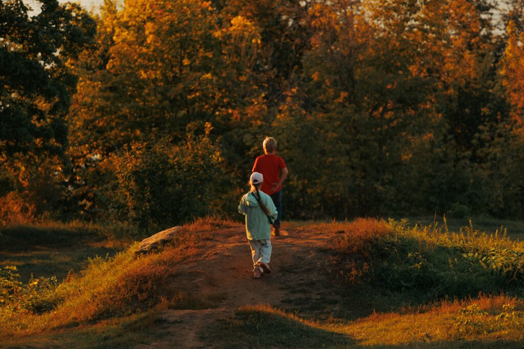 Two children hiking through an autumn forest, bathed in warm sunset glow, capturing the essence of fall.